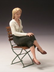 Eine junge Frau mit weißer Bluse und schwarzem Rock sitzt auf einem Klappstuhl.