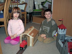 Foto: Zwei Kinder mit aus einem Karton gebastelten Lokschuppen, davor eine kleine rote Diesellok.