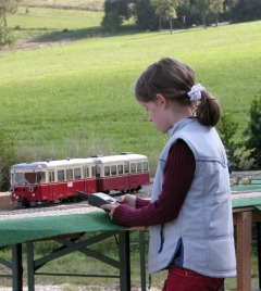 Ein Mädchen steuert mit einem Funkhandregler einen rot–beigen Triebwagen.