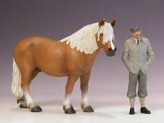 Ein Mann steht neben einer Pferde–Tierfigur von Schleich S.
