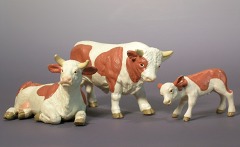 Braun–weiß gefleckte Tierfiguren: liegende Kuh, stehender Bulle und Kälbchen.
