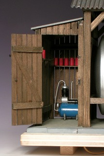 Ein Schuppen mit offener Tür, an der Wand gegenüber ein blauer Kompressor.