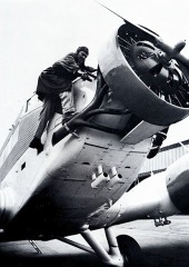 Foto mit Pilot mit einer Kurbel auf einer Leiter nahe dem mittleren Motor eines Flugzeugs.