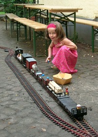 Ein kleines Mädchen in der Hocke spielt im Hof mit einem Zug auf den Gleisen.