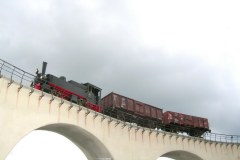 Dampflok Tssd 99 633 mit zwei Regelspurwagen auf Rollböcken auf einem Viadukt.