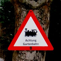 Verkehrsschild mit Dampflok–Symbol und Schriftzug „Achtung Gartenbahn”.