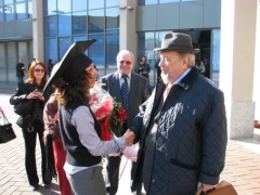 Ein bärtiger Mann mit Hut gratuliert einer Doktorantin auf einem Hof.
