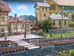 Detail eines Gartenbahn-Bahnhofs mit gemaltem Hintergrund auf einer Wand.