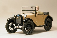 Modellfoto: kleines, offenes Auto mit ockerfarbener Karosserie und schwarzen Kotflügeln mit Fahrer–Figur.