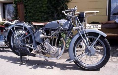 Graublaues, altes Motorrad mit Einzelsattel und vielen glänzend verchromten Teilen.