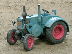 Graublauer Traktor mit hinteren Kotflügeln, Scheinwerfern und roten Felgen.