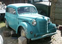 Foto: türkisfarbenes, zweitüriges Auto auf Schrottplatz.