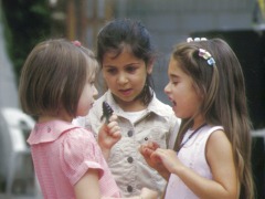 Zwei kleine Mädchen diskutieren miteinander, ein drittes hört zu.