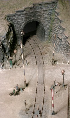 Modell: Bahnübergang mit weiß–blauer Schranke und Tunneleinfahrt dahinter.