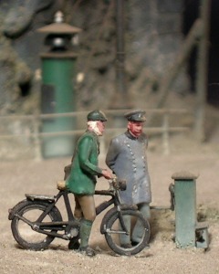 Modell: Zwei Männer am Bahnübergang, einer mit Fahrrad, einer ein Bahnbeamter.