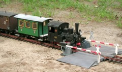 Ein Zug mit Dampflok, Personen– und Güterwagen durchfährt im Garten einen Bahnübergang.