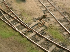 Eine Modell-Feldbahnweiche, daneben noch ein Gleis, im überwachsenen Gelände.