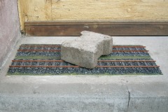 Zwei Gleisstücke von 60 cm Länge auf Sperrholz, mit einem Stein beschwert.