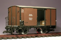 Modellfoto: Blick durch die geöffnete Tür eines gedeckten Güterwagens, im Laderaum steht eine Kiste.