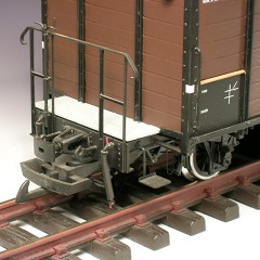 Stirnseite: gedeckter Güterwagen mit geschlitzter Pufferhülse und Bremsschläuchen.