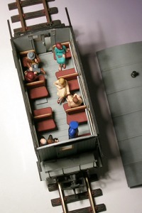 Modellfoto eines Reisezugwagens mit abgenommenem Dach, darin einige Figuren von Reisenden.