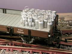 Ein Niederbordwagen, mit etlichen Milchkannen unterschiedlicher Größe beladen.