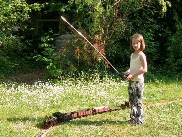 Ein Mädchen mit einem Funksender vor einem Modellzug im Garten.