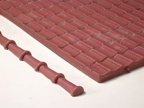 Ein rotbraunes Stück Dachplatte (Formziegel) und Firstziegel (nur teils sichtbar).