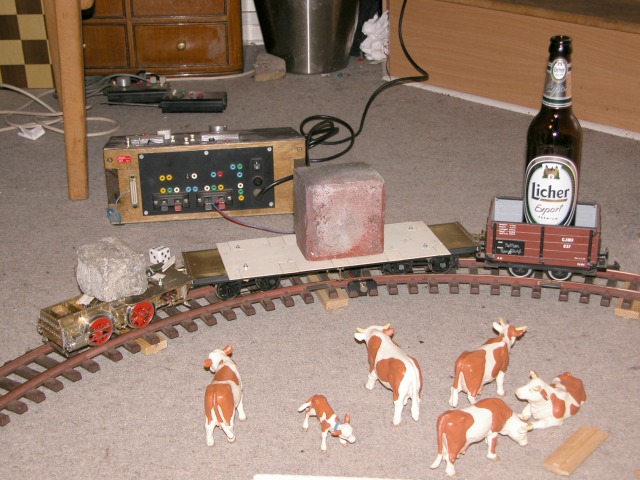 Lokfahrwerk mit Stein zieht einen Wagen mit einem halben Backstein darauf eine gebogene Rampe hinauf.