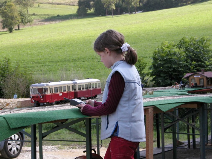 Ein Mädchen steuert mit einem Funkhandregler einen rot–creme–farbenen Triebwagen.