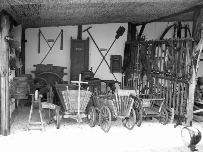 Landwirtschafts–Geräte um 1930: Wagen, Dreschflegel, Schleifbock, Pferdegeschirre.