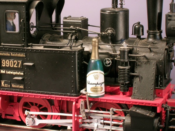 Eine Champagner–Flasche steht auf dem Umlauf einer Modell–Dampflok.