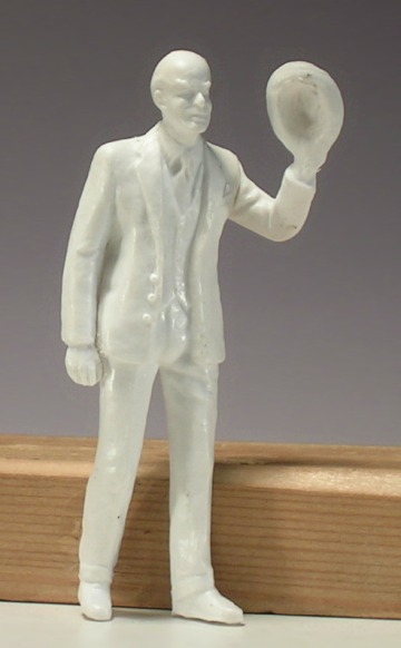 Modellfigur: Ein älterer Mann mit Glatze grüßt mit dem Hut in der linken Hand.