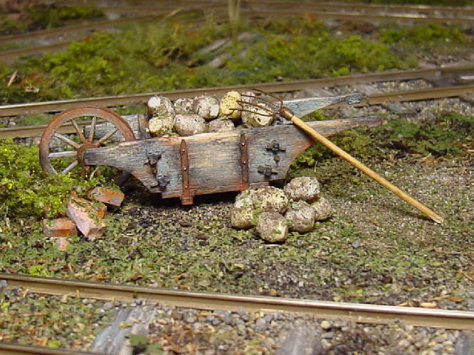 Alte Gartenkarre mit rostigen Beschlägen und Zuckerrüben darin zwischen zwei Feldbahngleisen.