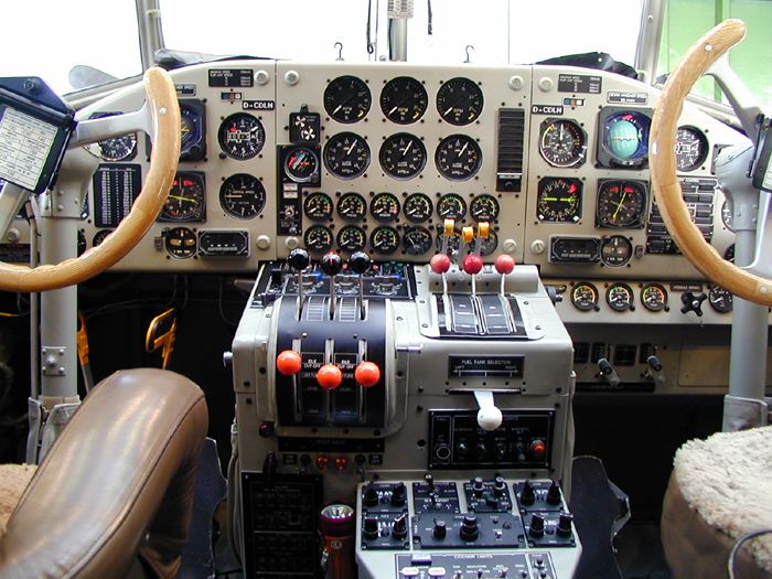 Blick in die Pilotenkanzel eines Flugzeugs mit Doppelsteuerung und vielen Instrumenten.