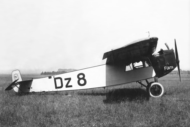 Foto: kleines Flugzeug von Fokker auf einer Wiese, von rechts.