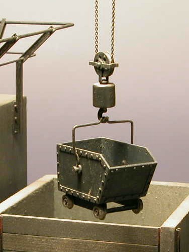 Ein Kohle–Hunt aus Blech hängt mit einem Bügel am Kranhaken.