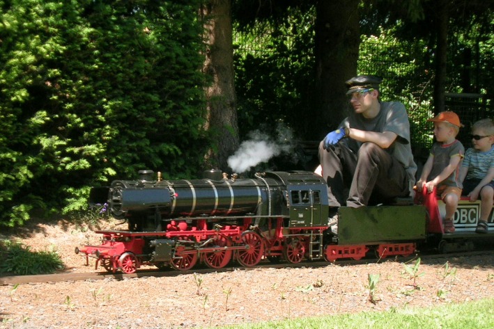 Eine große Dampflok mit Schlepptender, dahinter Kinder auf Sitzwagen.