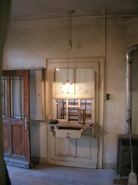 Blick in den Dienstraum im Bahnhof, eine Tür mit Ablage und Klappe im Fenster.