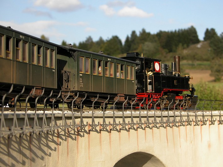 Echtdampflok mit zwei Personenwagen auf einem Viadukt vor einer echten Kulisse.