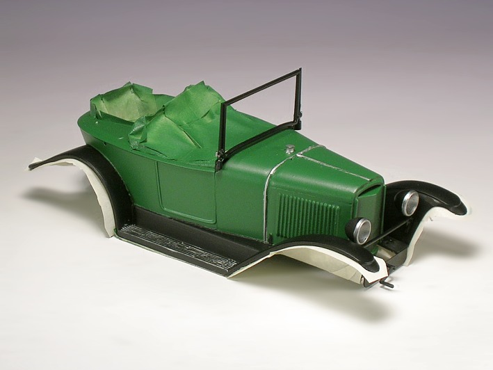 Die grün–schwarze Karosserie eine dreisitzigen Kleinwagen–Modells aus Kunststoff.