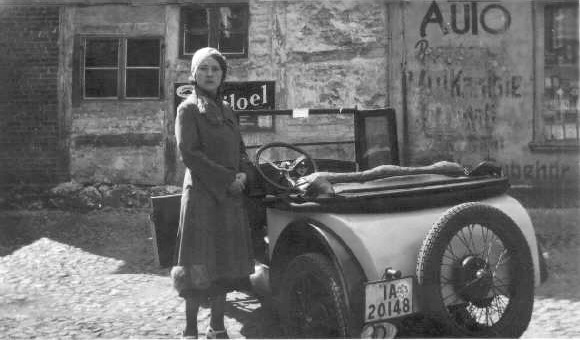 Eine junge Dame steht im Hofe einer Autowerkstatt neben ihrem Kleinwagen.