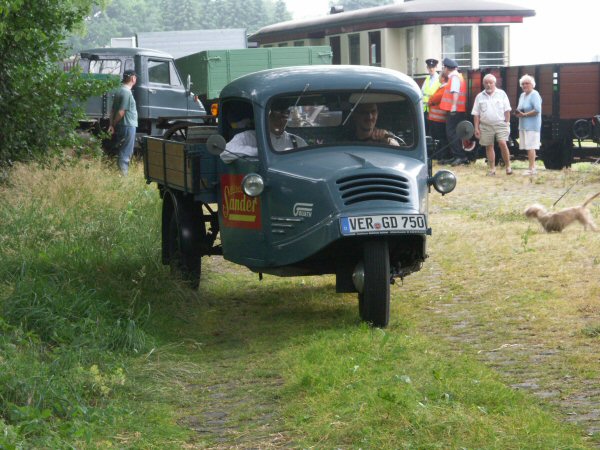 Graublaues Dreirad mit Hochpritsche bei einer Museumseisenbahn, von vorne.