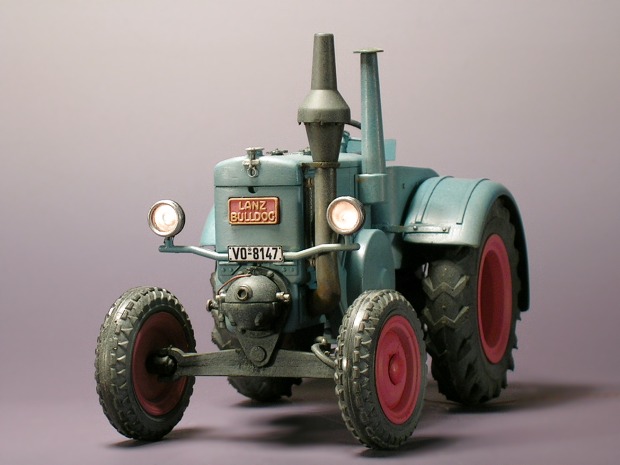 Fertig montiertes Traktormodell im Halbdunkel, mit leuchtenden Scheinwerfern von vorne gesehen.