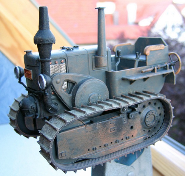 Modellfoto: hell graublauer Traktor mit Raupenketten am offenen Fenster.
