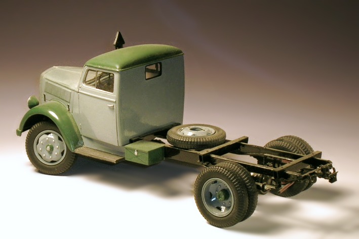 Modellfoto: grauer Lastkraftwagen mit grünen Kotflügel, noch ohne Pritschenaufbau und hintere Kotflügel.