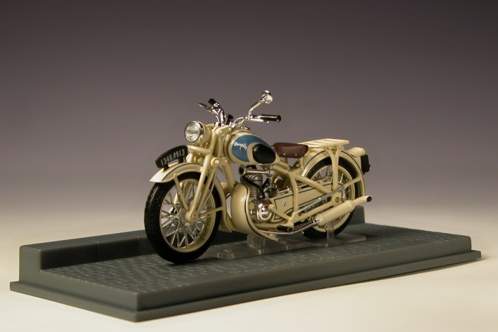 Ein helles Motorrad–Modell mit Beinschilden auf einem Ausstellungssockel.