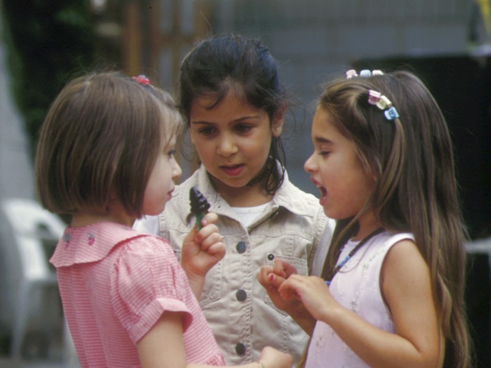Zwei kleine Mädchen diskutieren miteinander, ein drittes hört zu.