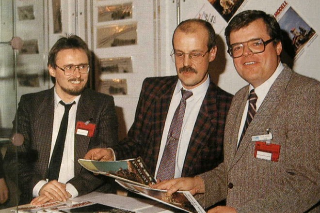 Drei Männer betrachten Modellbahn–Fachzeitschriften.