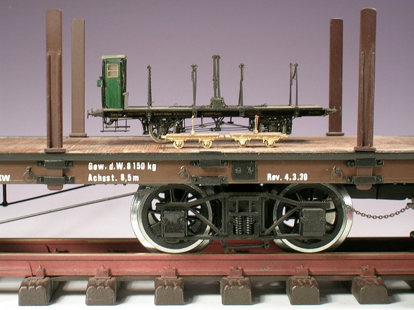Auf dem Schienenwagen stehen ein kleinerer Rungenwagen, davor zwei noch kleinere Drehschemelwagen.